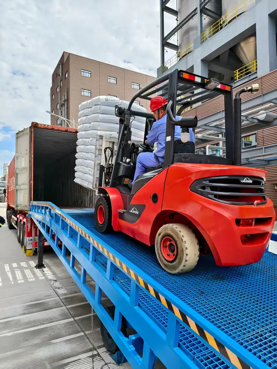 Forklift carrying a pallet of 25 kg plastic resin bags up a ramp into a shipping container
